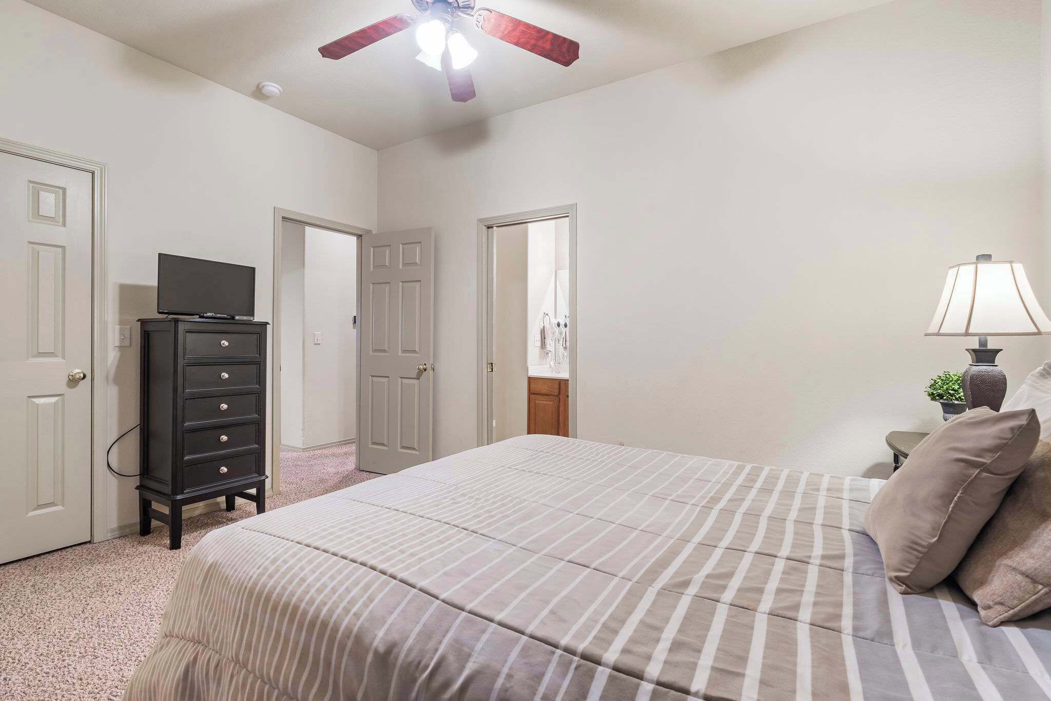 A bedroom with a bed, dresser, TV, lamp, and ceiling fan.