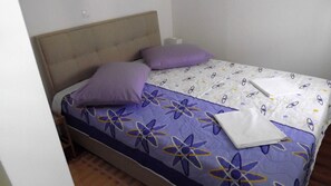 A single bed with a headboard, a purple pillow, a folded white towel, and a patterned bedspread. - Apartment 9 With a Double bed (Split)