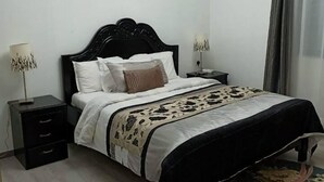 A bedroom with a bed, nightstands, a lamp, a floral rug, and two framed pictures on the wall. - Beautiful 2-bed Apartment in Nairobi (Nairobi)