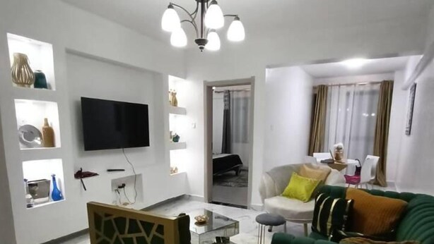A modern living room with a flat-screen TV, a green sofa, a coffee table, and a decorative screen. - Beautiful 2-bed Apartment in Nairobi (Nairobi)