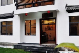 Um edifício com estilo arquitetônico tradicional chinês, apresentando uma varanda com guarda-corpo, uma porta com janela e uma pequena área de jardim na frente.