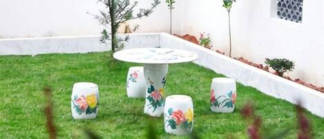 Ein Garten mit einem runden Tisch und vier Stühlen, umgeben von einer weißen Mauer und kleinen Pflanzen.