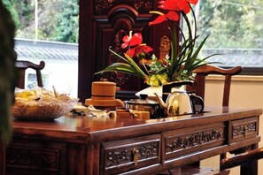 A wooden table with a vase of red flowers, a bowl of bread, and various kitchen items. - Huashu Theme Inn (Wuyuan)