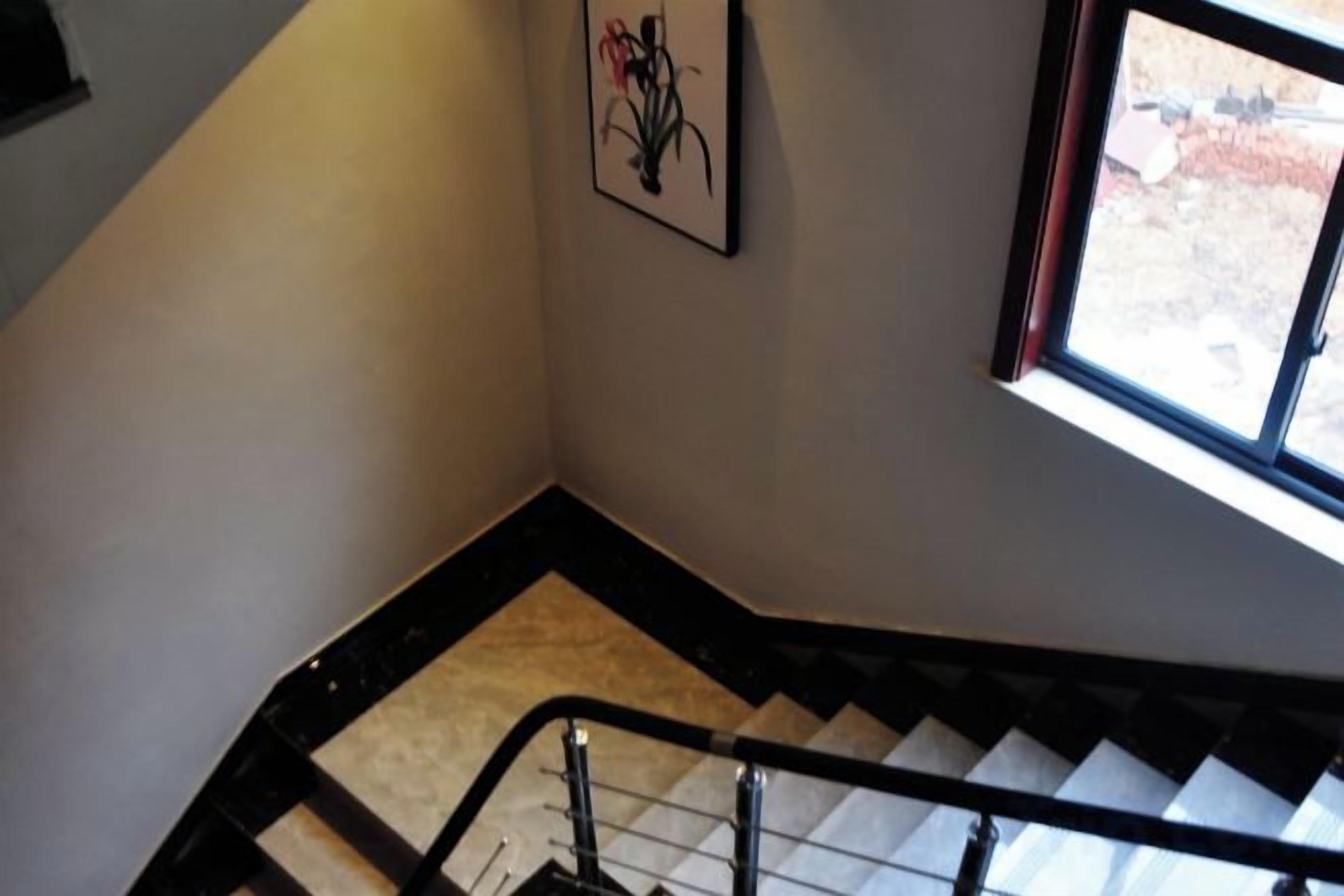 Una escalera con barandilla, un cuadro enmarcado en la pared y una ventana que da a vistas del exterior.