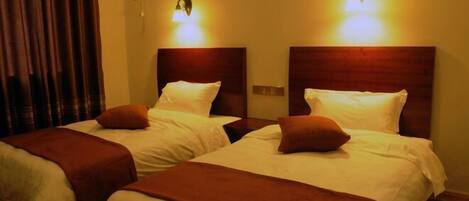 Two beds with headboards, a curtain, and wall-mounted lights.