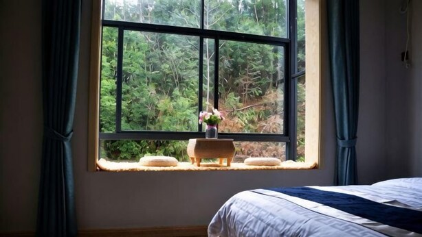 A bedroom with a large window, a bed, and a small stool with a vase. - Huashu Theme Inn (Wuyuan)
