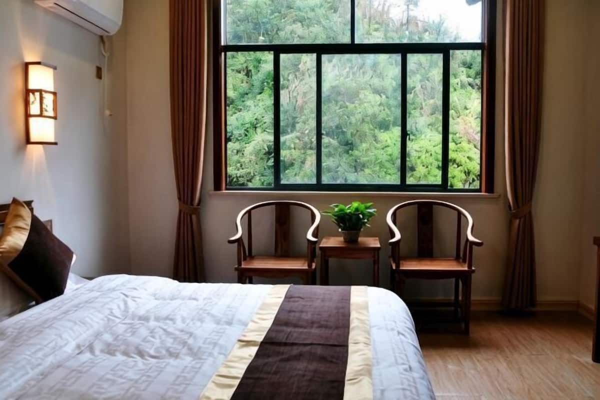 Ein Schlafzimmer mit großem Fenster, einem Bett, zwei Stühlen und einem kleinen Tisch mit einer Pflanze.