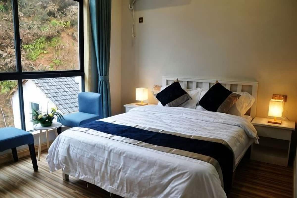 Ein Hotelzimmer mit einem großen Bett, zwei Nachttischen, einem Sessel und Blick auf Grünflächen.