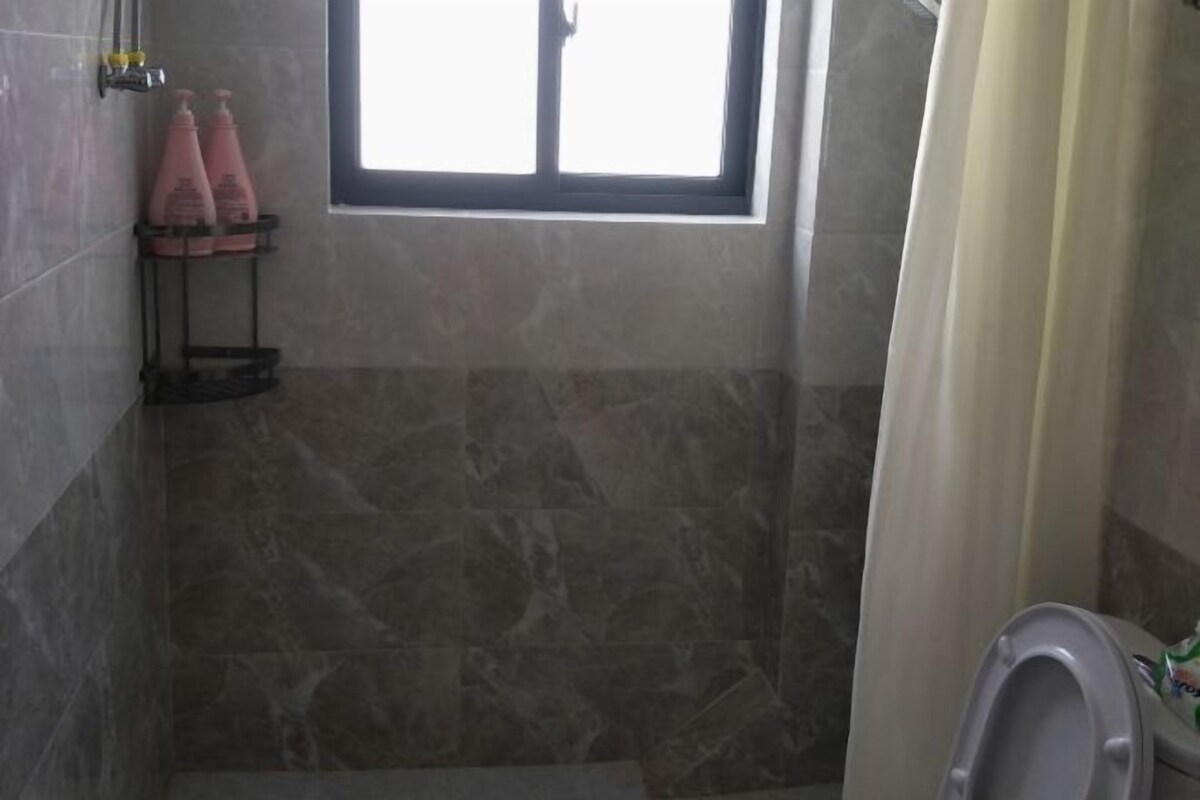 A bathroom with a shower area, a toilet, and a window.