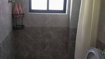 Un baño con zona de ducha, inodoro y ventana.