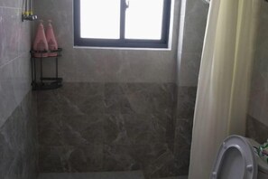 A bathroom with a shower area, a toilet, and a window. - Huashu Theme Inn (Wuyuan)
