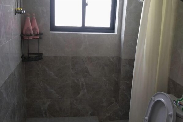 A bathroom with a shower area, a toilet, and a window. - Huashu Theme Inn (Wuyuan)