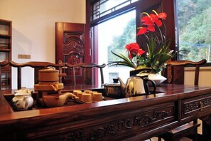 A wooden table with a vase of red flowers, a teapot, and various tea cups. - Huashu Theme Inn (Wuyuan)