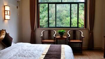 A bedroom with a large window, a bed, two chairs, and a small table with a plant.