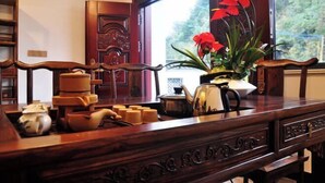 A wooden table with a vase of red flowers, a teapot, and stacked teacups. - Huashu Theme Inn (Wuyuan)