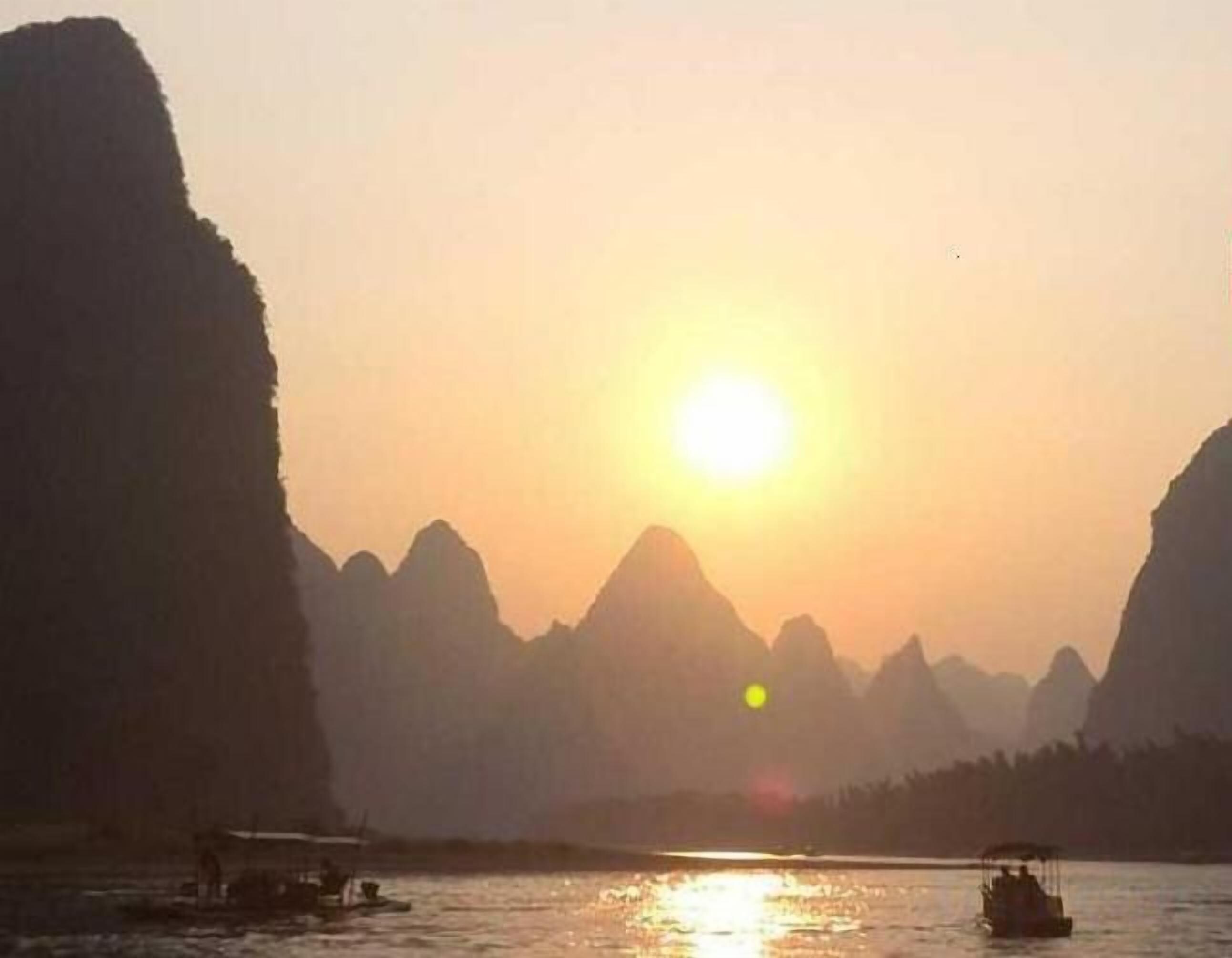 Un coucher de soleil sur une étendue d'eau, avec des montagnes en arrière-plan.