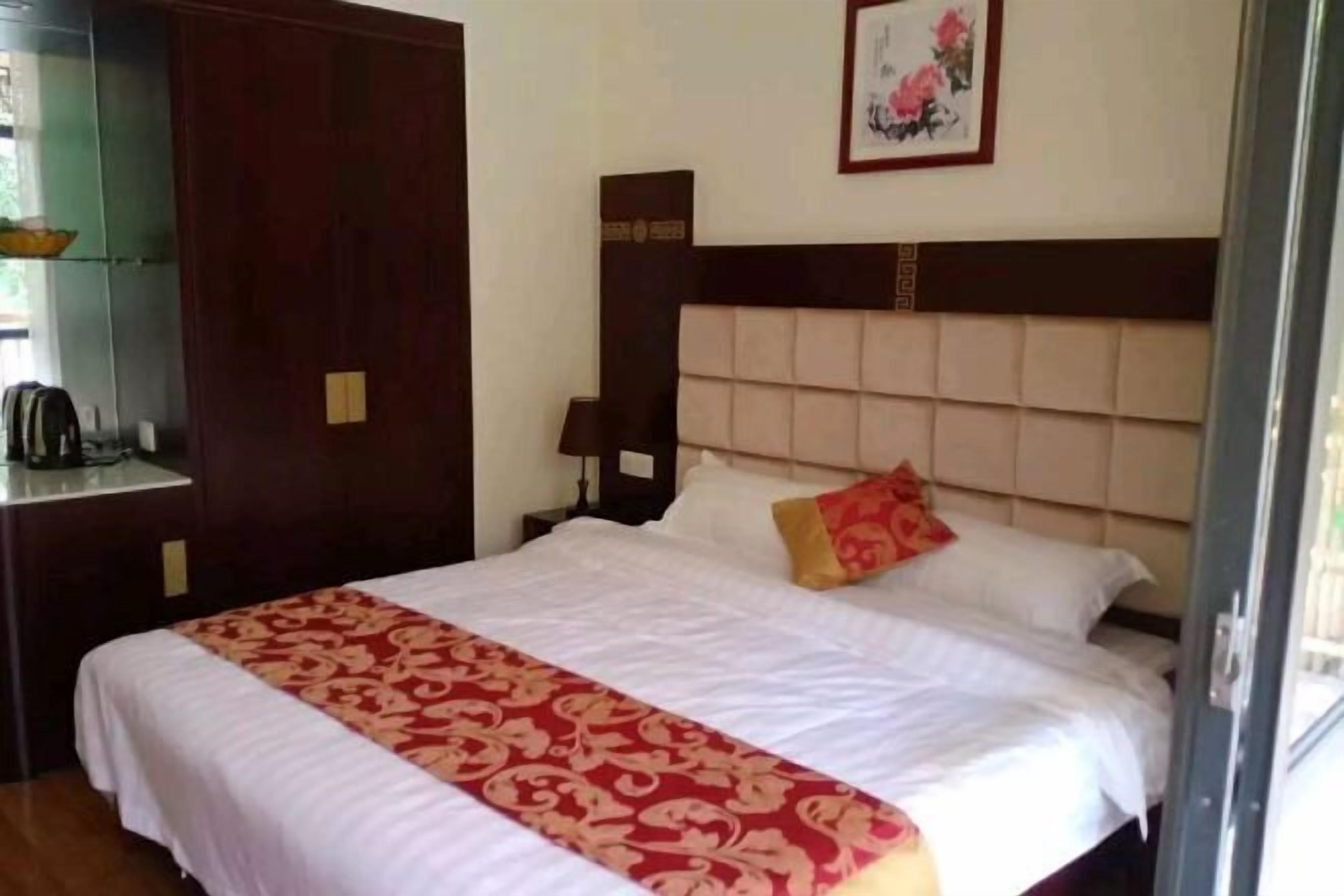 A hotel room with a large bed, a wooden wardrobe, a nightstand, and a framed picture on the wall.