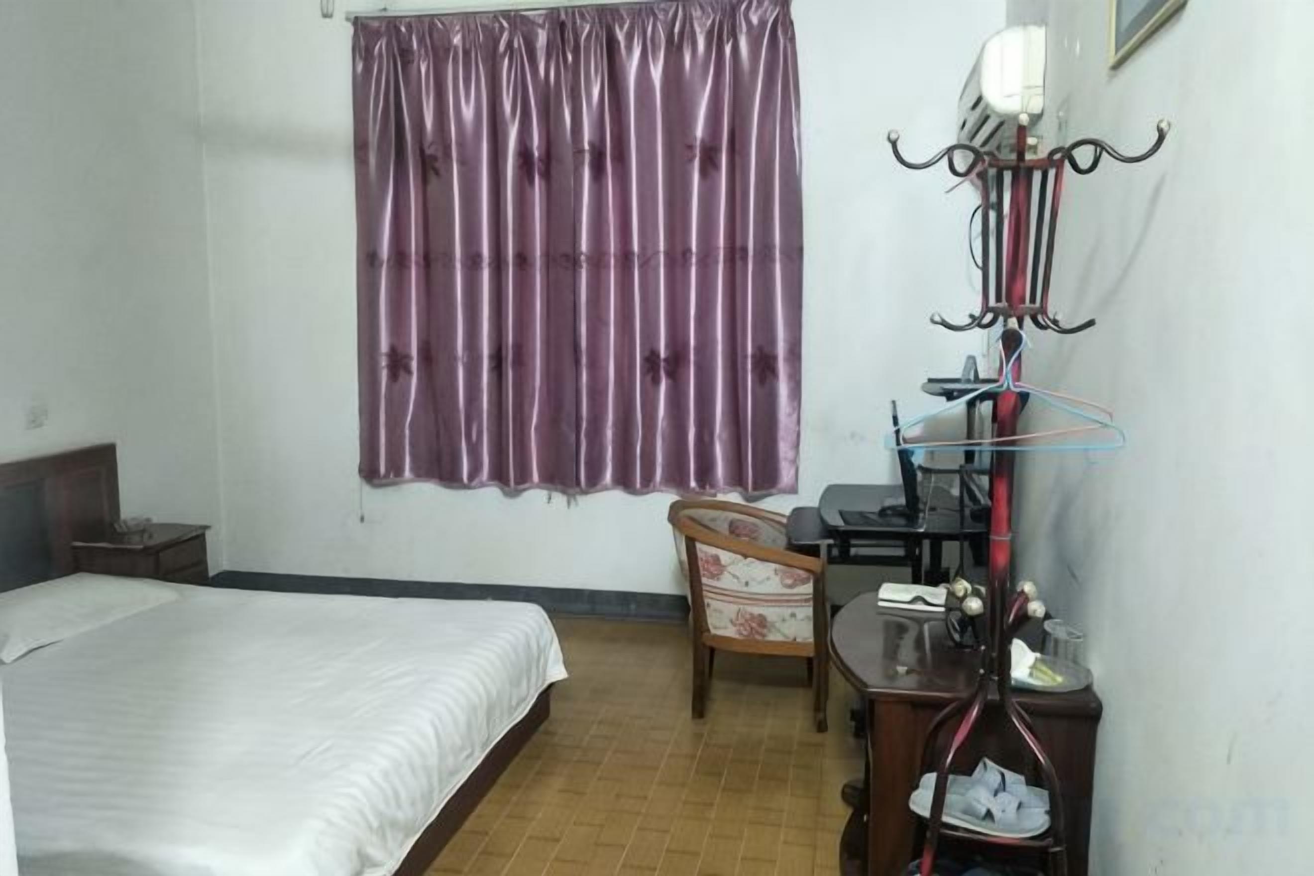 A bedroom with a bed, a chair, a desk, and a window with curtains.