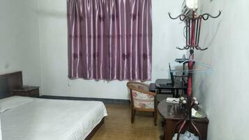 A bedroom with a bed, a chair, a desk, and a window with curtains.