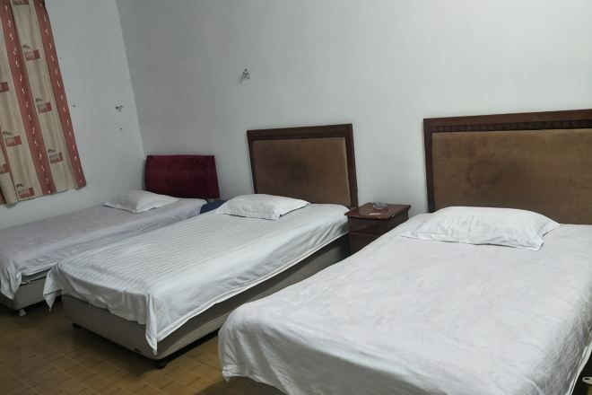 Habitación de hotel con tres camas individuales, cabecera de madera, una silla roja y una mesita.