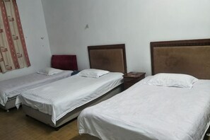 A hotel room with three single beds, a wooden headboard, a red chair, and a small table. - Kangfulai Hotel (Shengzhou)