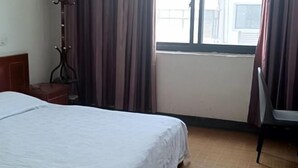 A hotel room with a bed, a chair, a coat rack, and a window with curtains. - Kangfulai Hotel (Shengzhou)