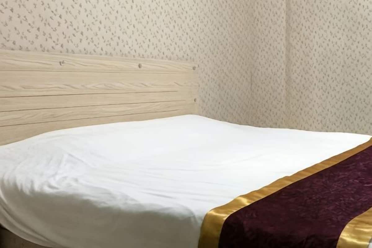 A single bed with a wooden headboard, a white mattress, and a purple and gold decorative border.