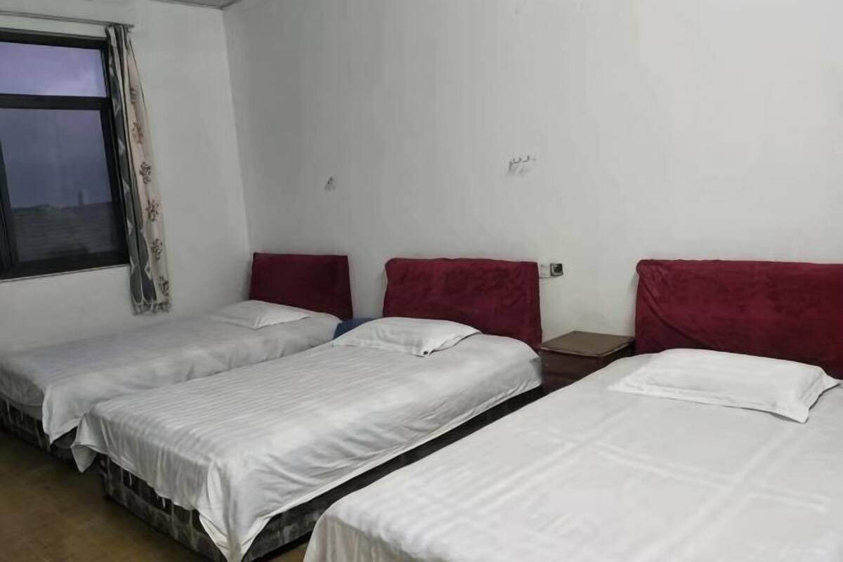 A room with three single beds, each with a red headboard, white bedding, and a window with curtains.