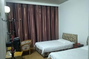 A hotel room with two beds, a desk, a chair, and a lamp. - Kangfulai Hotel (Shengzhou)