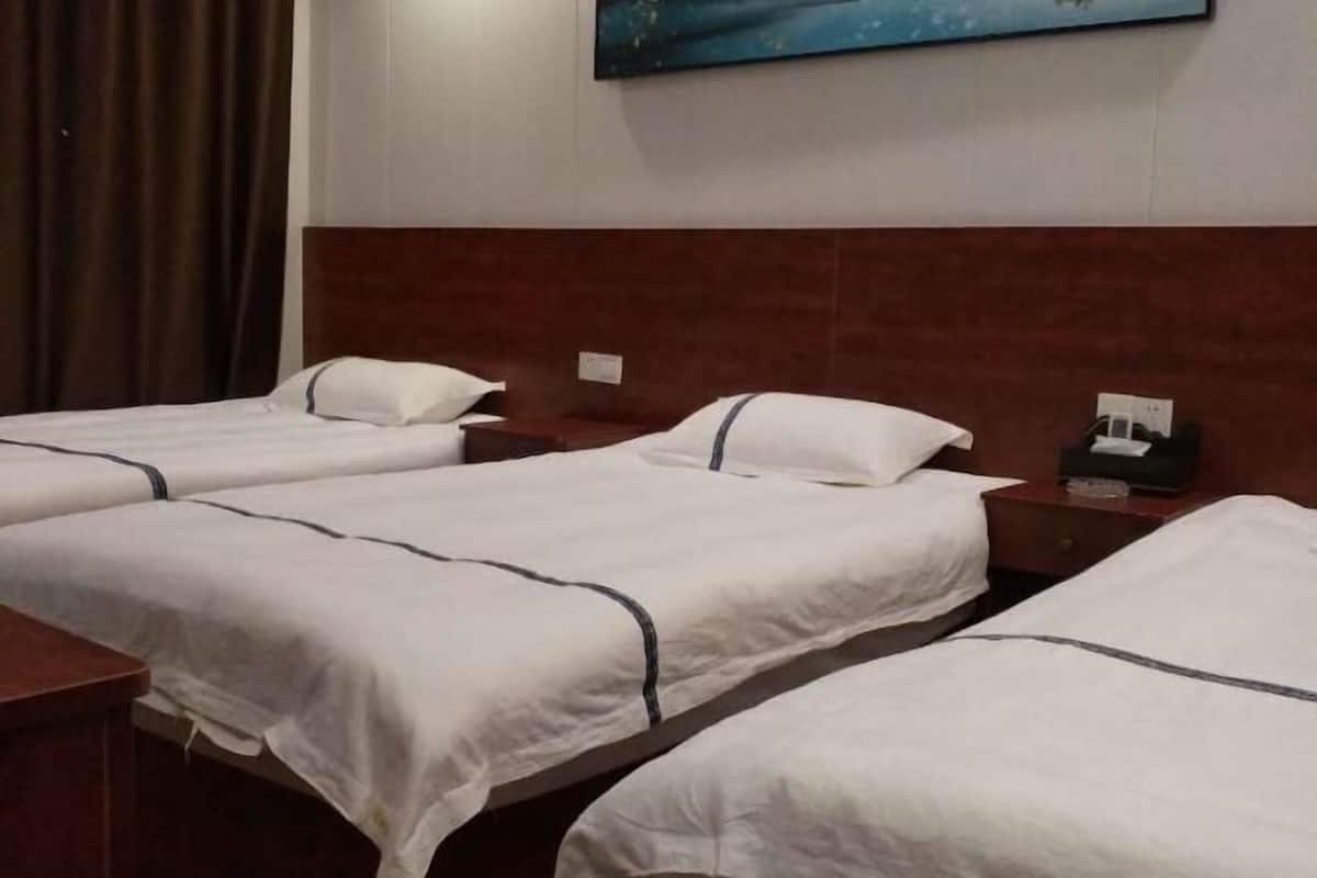 Habitación de hotel con tres camas individuales, cabeceros de madera, una cortina marrón y un cuadro en la pared.