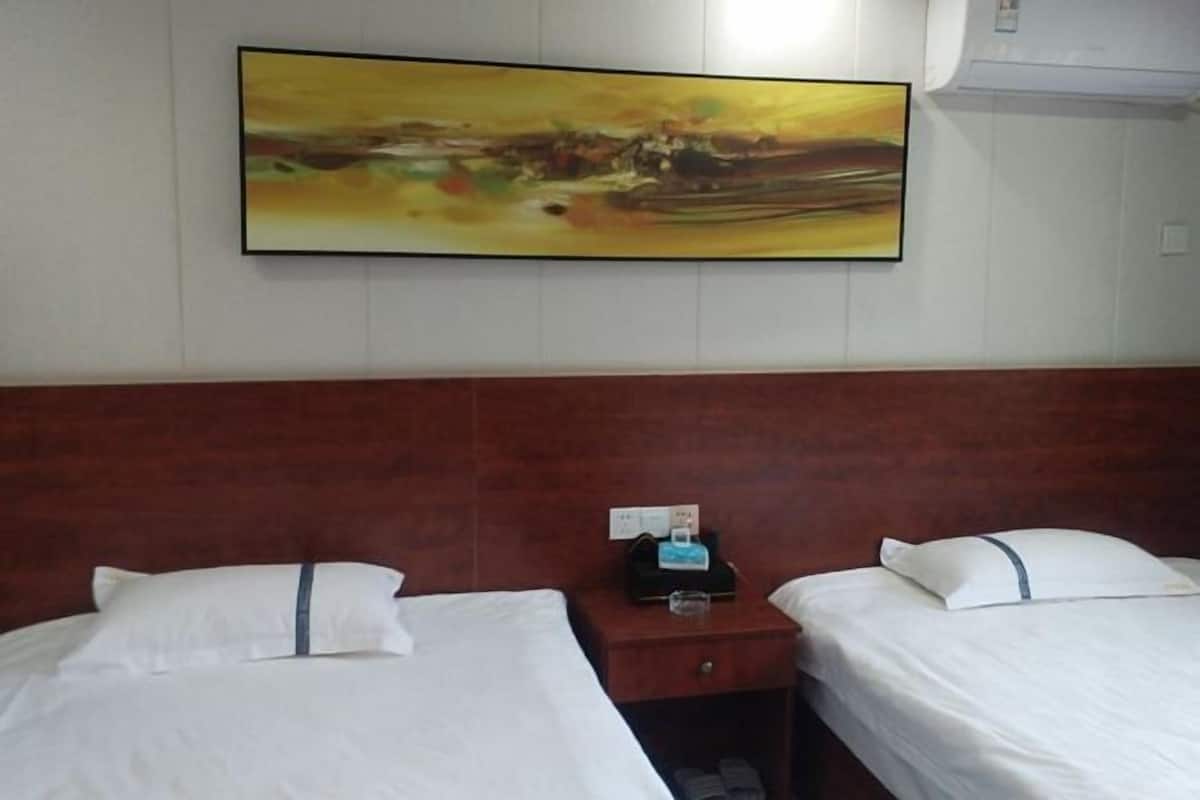 Habitación de hotel con dos camas, cabecero de madera, un cuadro en la pared y mesita de noche con un teléfono y un vaso.