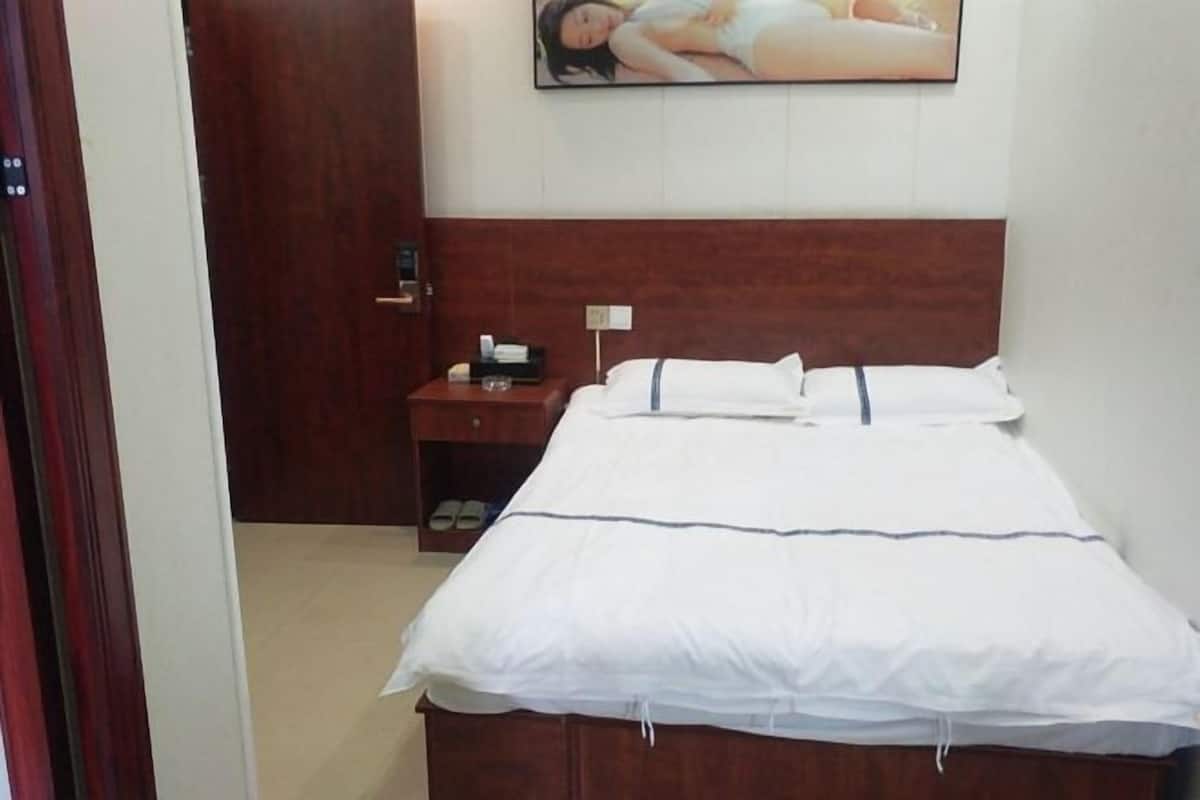 Una habitación de hotel con cabecera de madera, cama con ropa de cama blanca, mesita de noche con lámpara y un cuadro en la pared.