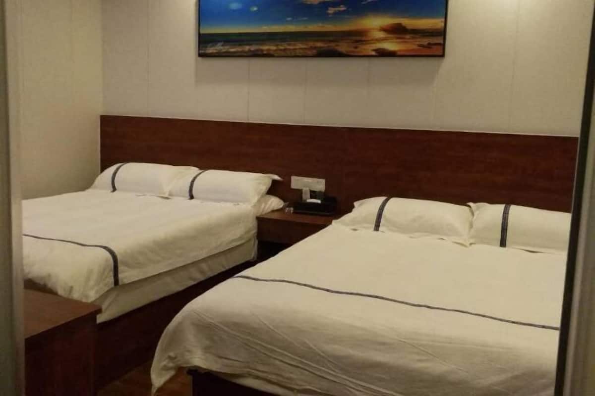 Habitación de hotel con dos camas, una mesita de noche, un cuadro de un paisaje y un cabecero de madera.