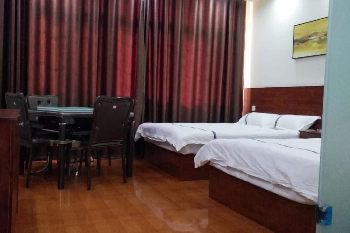 Una habitación con piso de madera, un escritorio con sillas, una cama con ropa de cama blanca y una cortina.