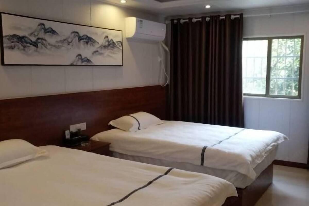 Habitación de hotel con dos camas, un cuadro, un equipo de aire acondicionado, una ventana con cortinas y una mesita de noche con lámpara.