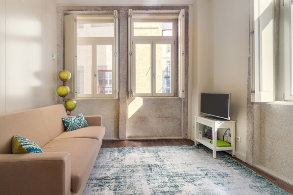 A living room with a beige sofa, a television on a stand, and a patterned rug. - Oporto Home River Front (Porto)