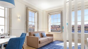 Una sala de estar moderna con un sofá color beige, sillones azules y un amplio ventanal con vistas a la ciudad.