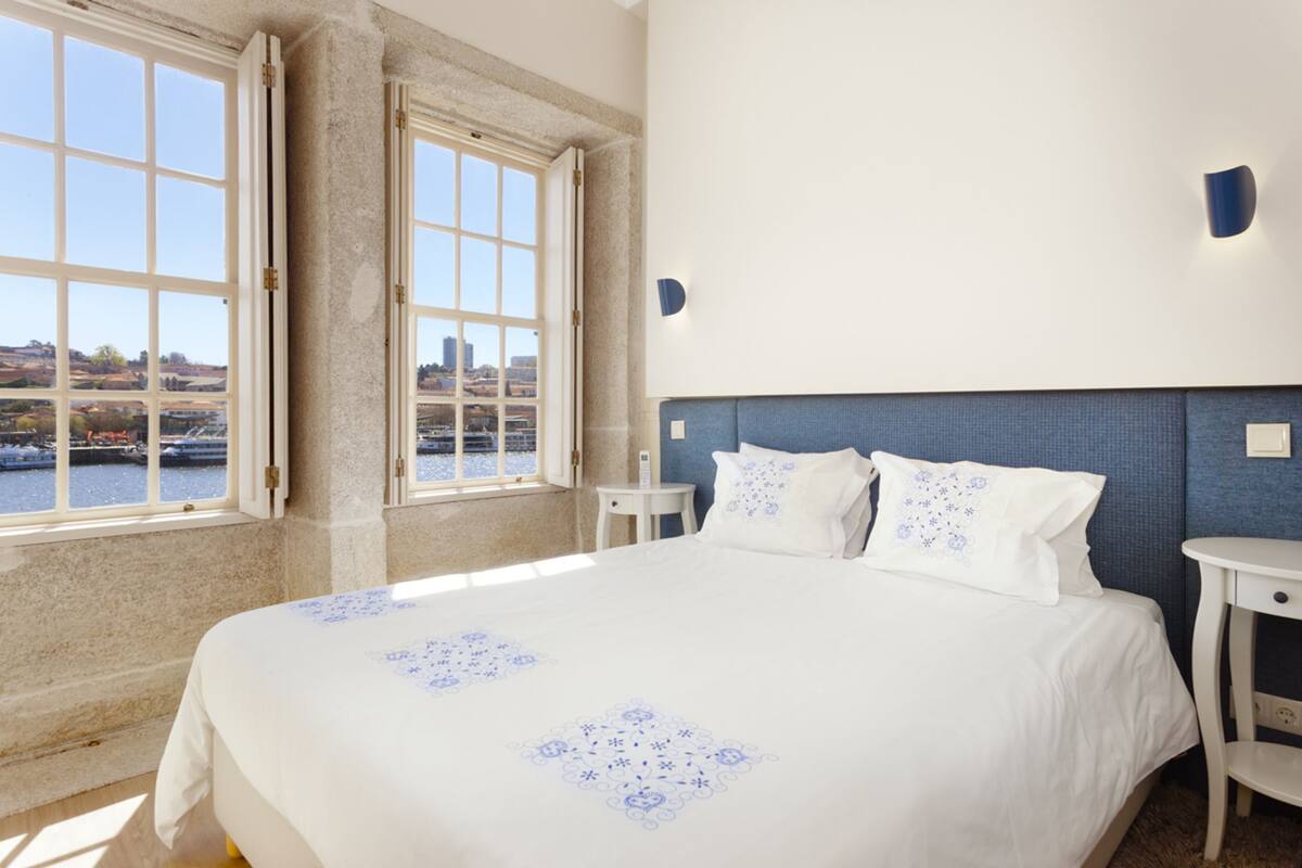 A hotel room with a large bed, a view of a river, and a cityscape.