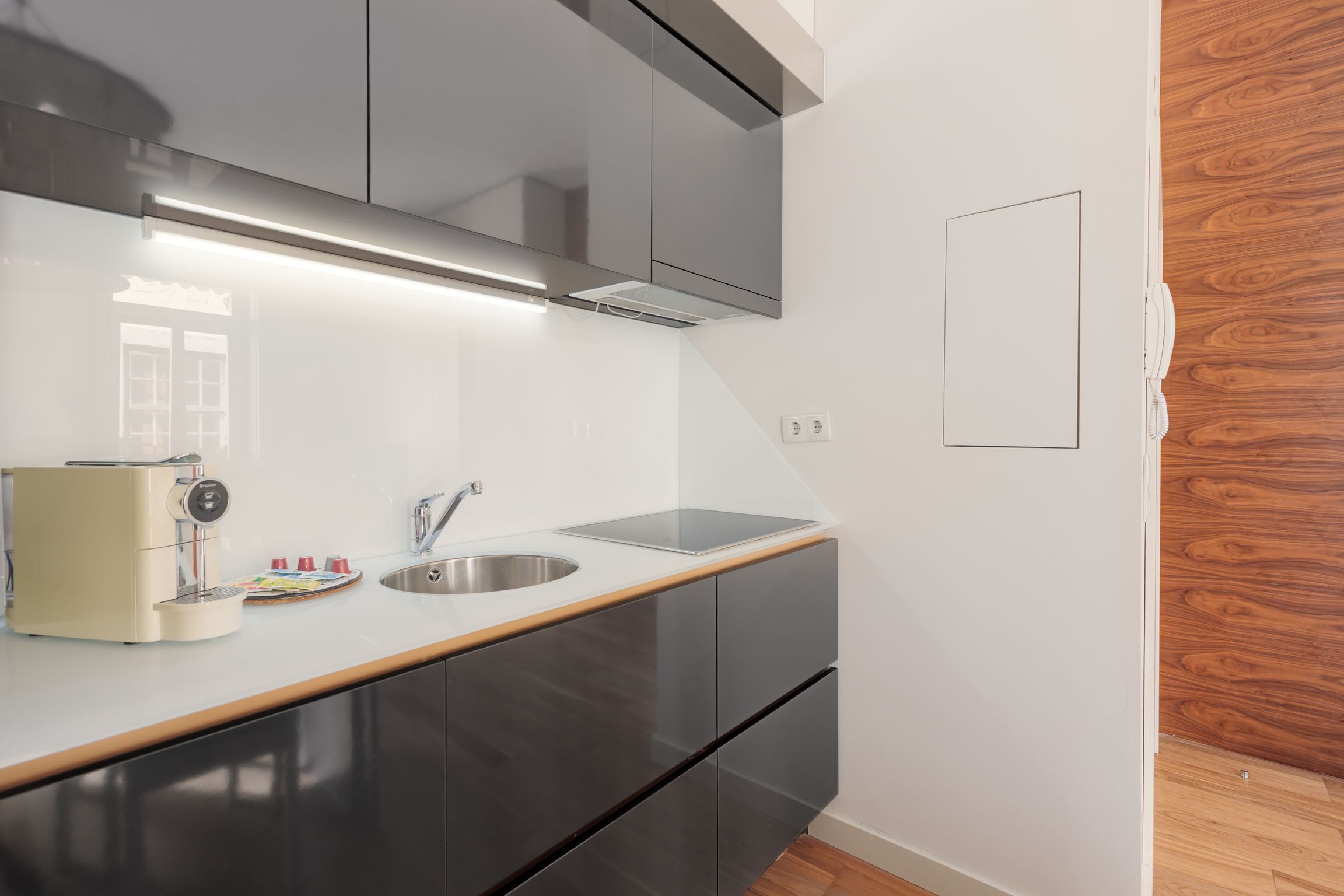 A modern kitchen with a stainless steel sink, a coffee machine, and wooden flooring.