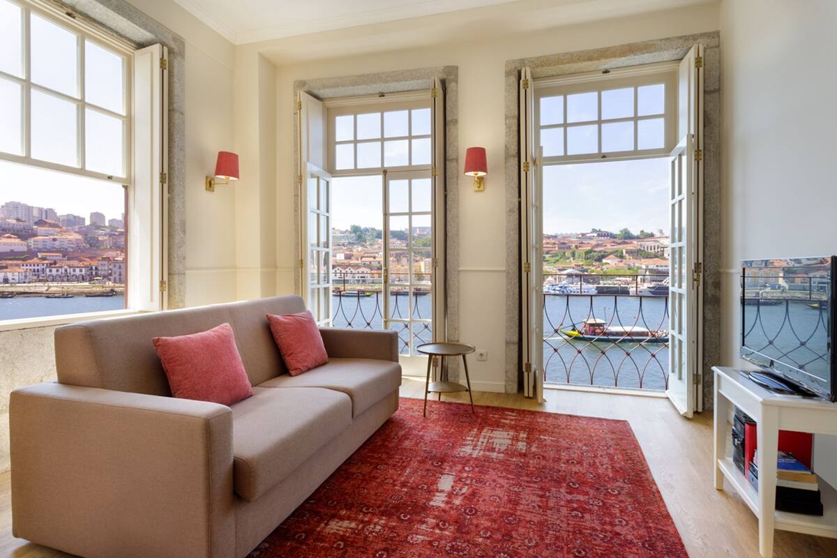 A living room with a sofa, red rug, and a view of a cityscape through large windows.