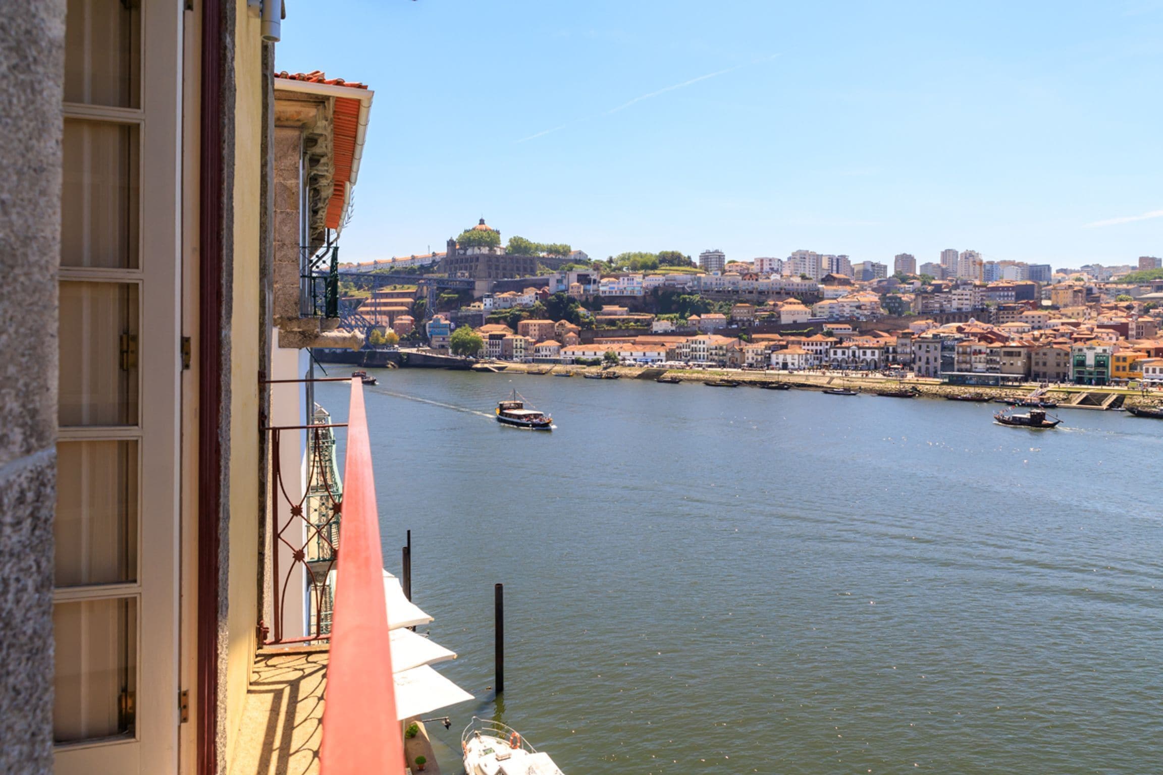 Vista de un río con barcos, un paisaje urbano al fondo y un edificio con balcones.