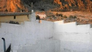 Une cour avec un mur blanc, une petite table, une chaise et un pot de fleurs.