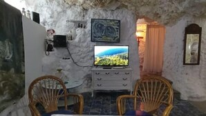 Una habitación con televisor sobre un tocador blanco, dos sillas de mimbre, un cuadro en la pared y un espejo.