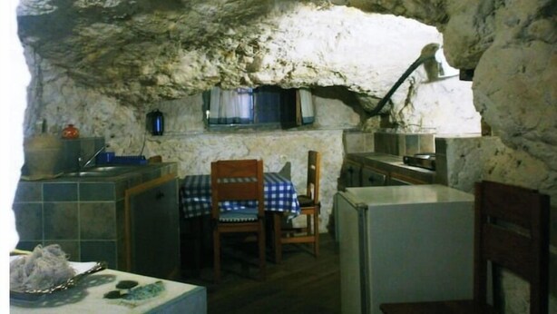 Una cocina rústica con paredes de piedra, una mesa de madera, sillas y electrodomésticos básicos.