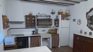 Cocina compacta con isla central, horno empotrado y refrigerador. Cuenta con gabinetes de madera y un perchero con vajilla.