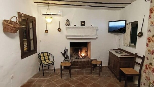 Una sala de estar acogedora con chimenea, dos sillones, un televisor y un aparador de madera.