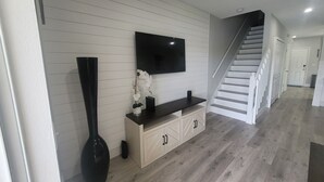 Een moderne woonkamer met een flatscreen televisie aan de muur, een donker houten console tafel en een hoge zwarte vaas.