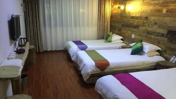 A hotel room with three beds, wooden flooring, a wooden wall, a TV, and a curtain.