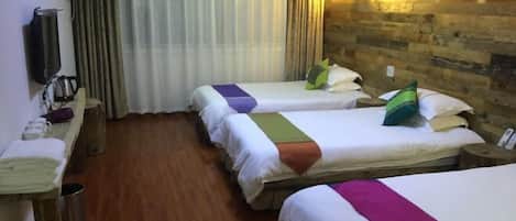 A hotel room with three beds, wooden flooring, a wooden wall, a TV, and a curtain.