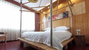 A wooden four-poster bed with white linens, a wooden bench, and a small bedside table in a room with wooden walls and a large window.